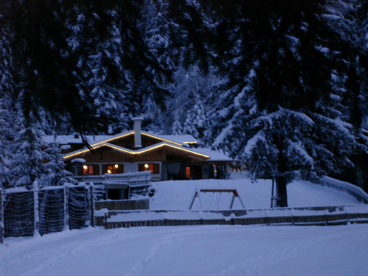 Happi's Hütte im Winter bei Dämmerung mit Lichterkette — Tiroler Hütte zwischen verschneiten Fichten in Tarrenz