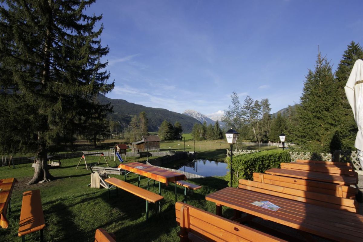 Sommerterrasse der Happi's Hütte mit Holzbänken, Spielplatz und Bergblick im Gurgltal
