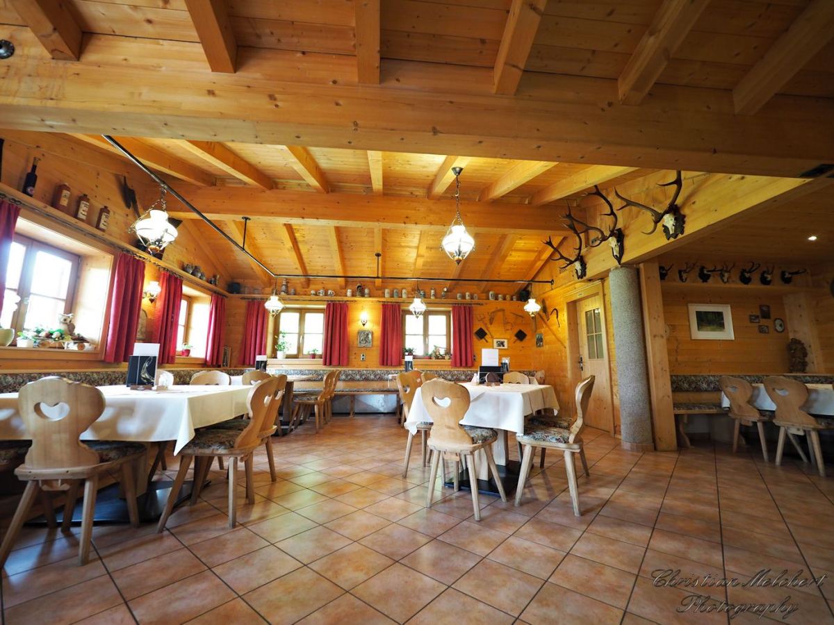 Gastraum der Happi's Hütte — Tiroler Wirtsstube mit Holzbalken, weißen Tischdecken und Hirschgeweih