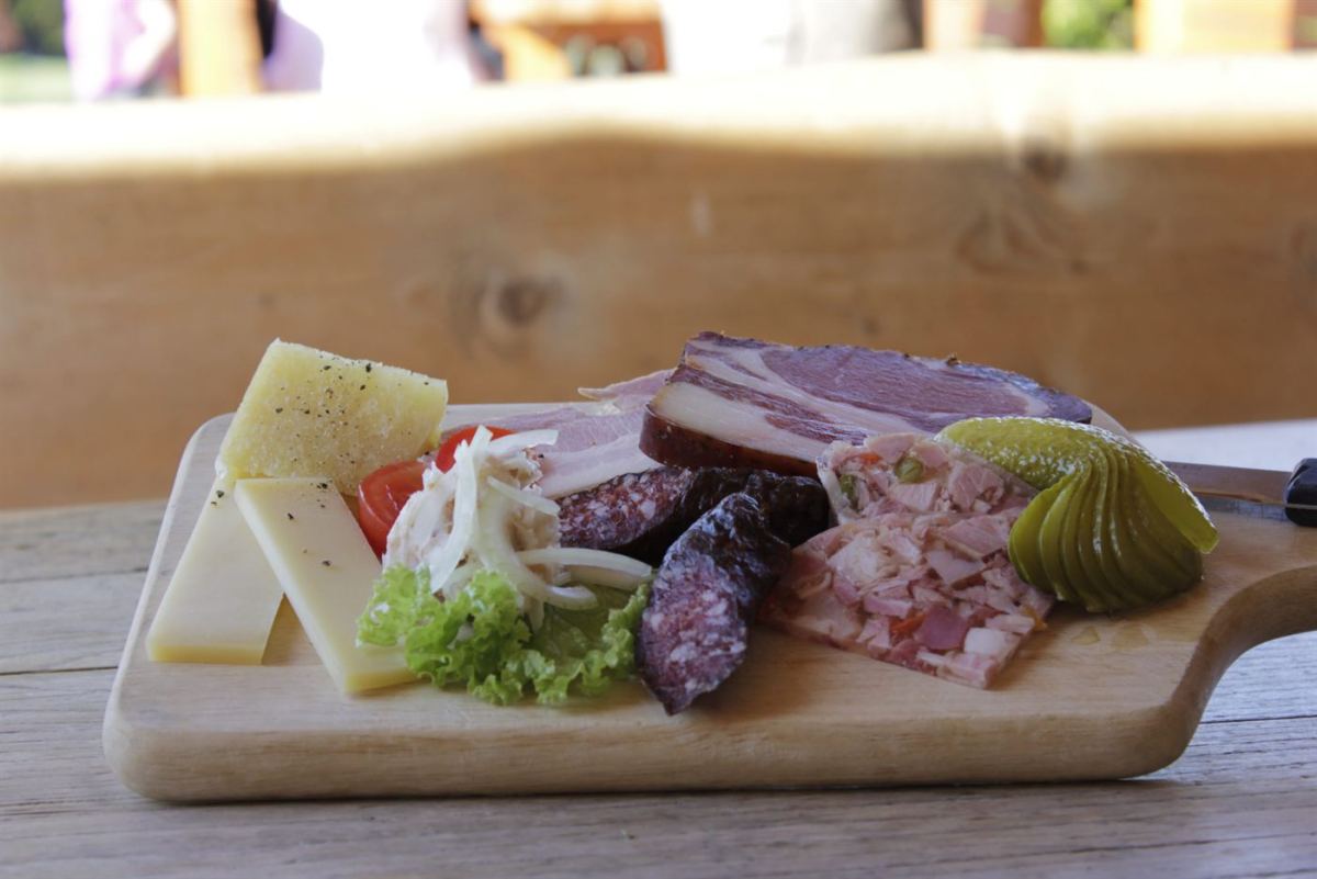 Tiroler Brettljause mit Speck, Käse, Hauswurst, Salat und Essiggurken auf Holzbrett bei Happi's Hütte